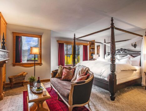 A four-poster bed sits behind a large sitting area with a fireplace.